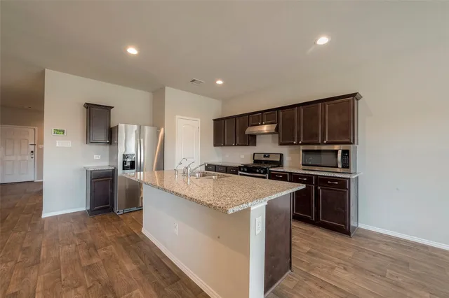 a kitchen with stainless steel appliances a stove top oven a sink a refrigerator white cabinets and wooden floor