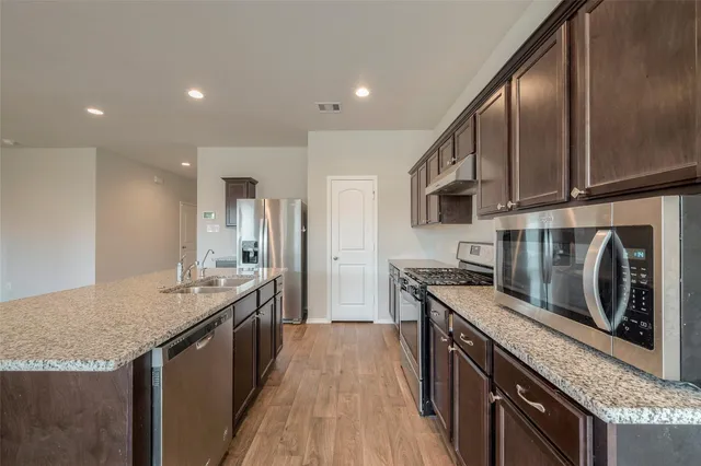 a kitchen with stainless steel appliances granite countertop a kitchen island a stove a refrigerator and a sink