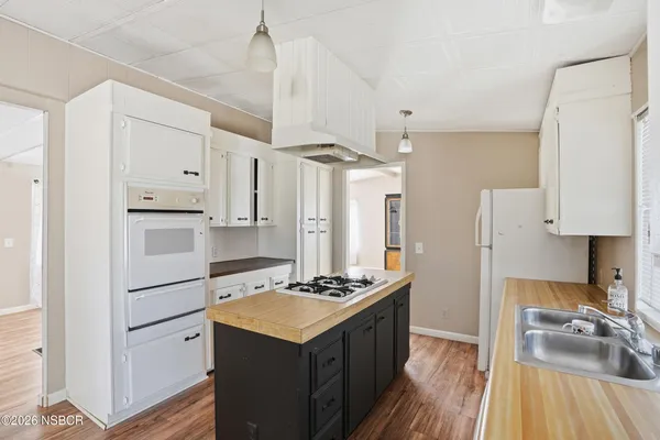 a kitchen with granite countertop a refrigerator stove a sink dishwasher and white cabinets with wooden floor