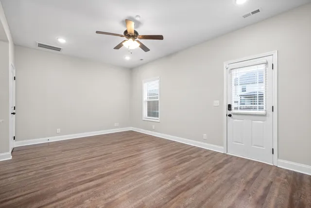 a view of an empty room with wooden floor and a ceiling fan