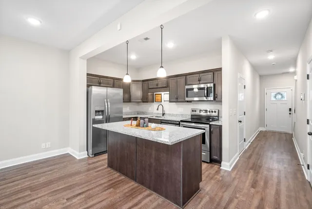 a kitchen with stainless steel appliances granite countertop a refrigerator a sink dishwasher a stove and white countertops with wooden floor