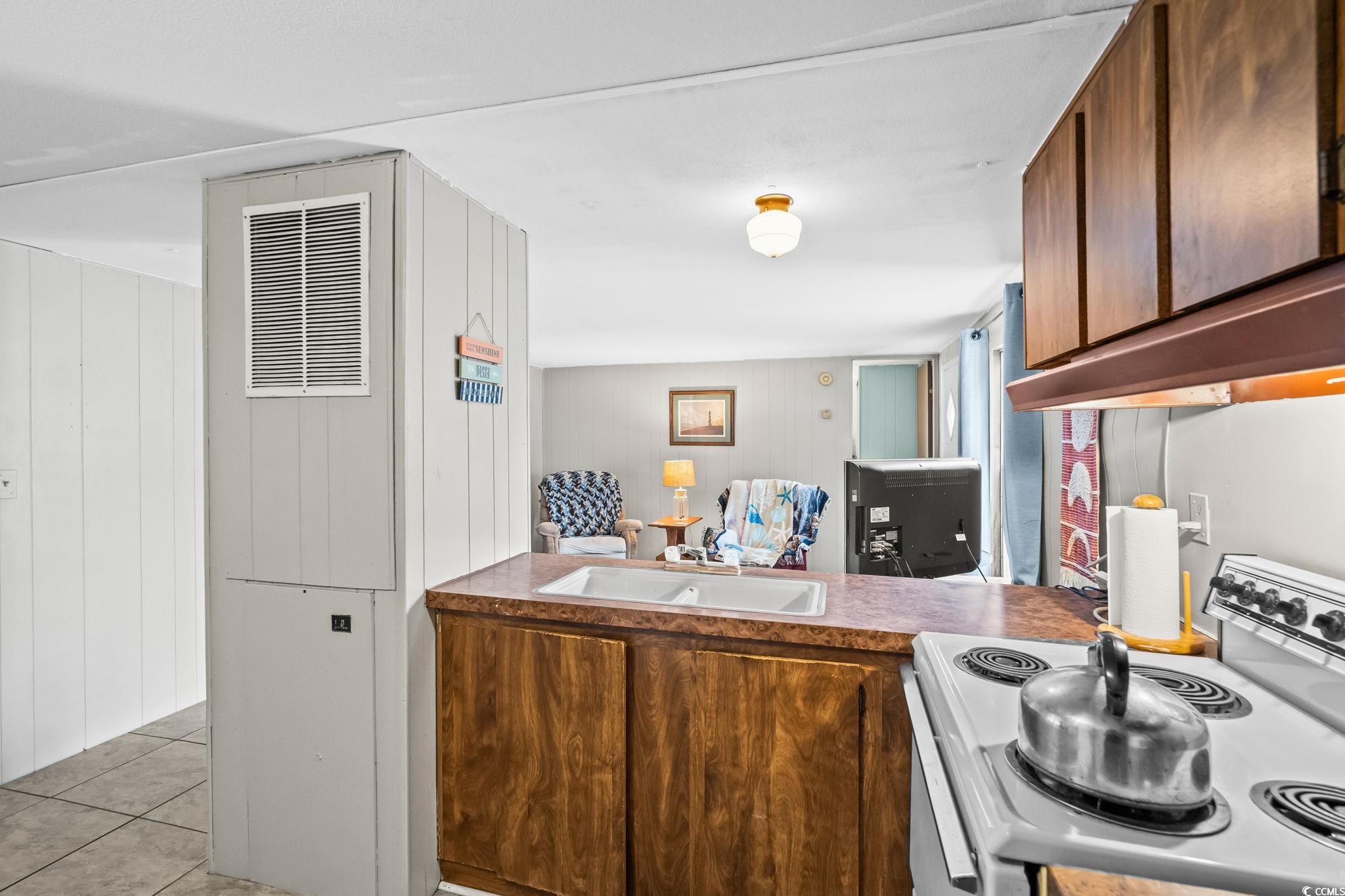 4516 Willet Street North Myrtle Beach, SC 29582 - Photo 18 of 40 Kitchen featuring electric stove, light tile patterned floors, wooden walls, and brown cabinetry