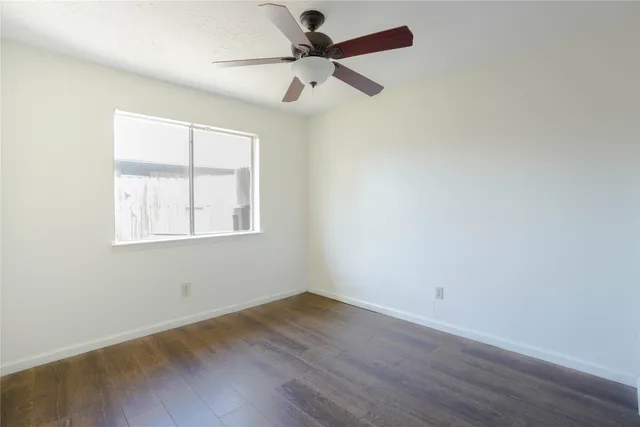 an empty room with wooden floor ceiling fan and windows