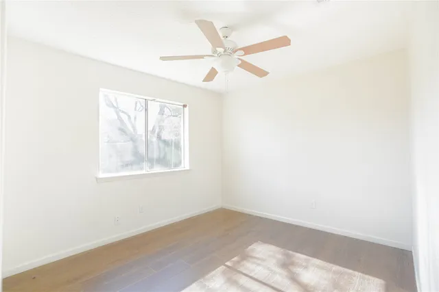 an empty room with wooden floor fan and windows