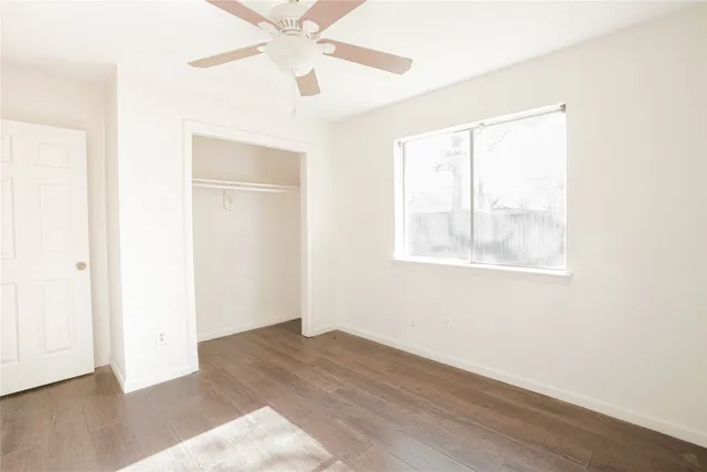 an empty room with wooden floor chandelier fan and windows