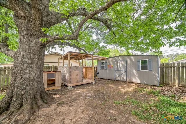 a view of a barn in the backyard with large tree and wooden fence
