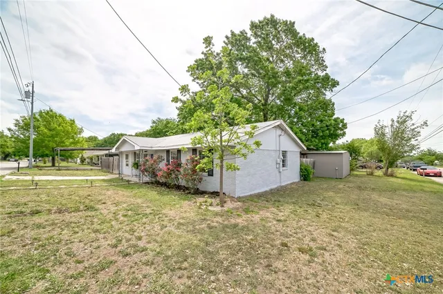 a view of a wooden house with a big yard and large trees