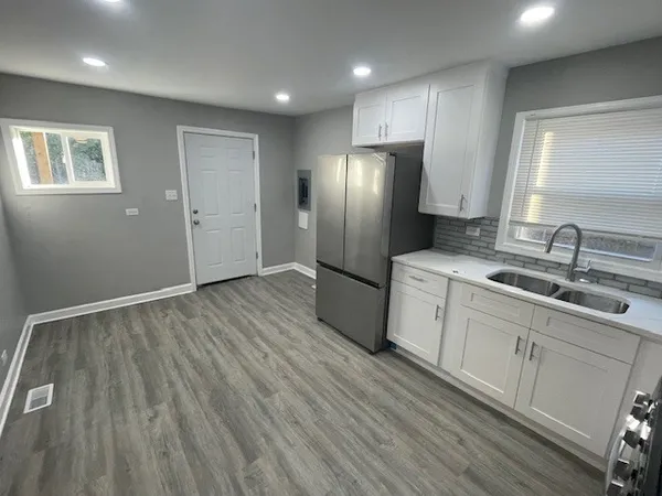 a kitchen with stainless steel appliances granite countertop a refrigerator a sink and white cabinets with wooden floor