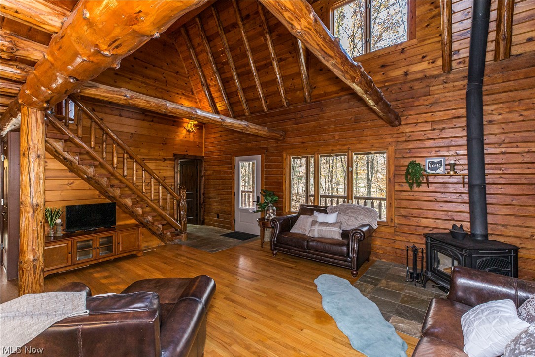Living room featuring wooden walls, a wood stove, high vaulted ceiling, and hardwood / wood-style flooring