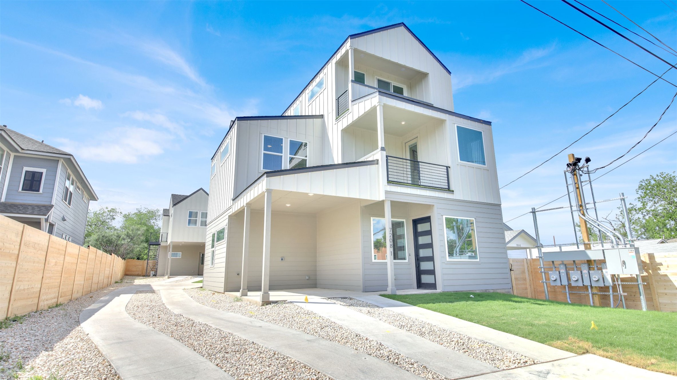 7208 Providence Avenue, Unit 1 Austin, TX 78752 - Photo 1 of 26 Modern three-story property featuring light-colored siding, a black front door with frosted glass panels, and a concrete driveway with gravel accents