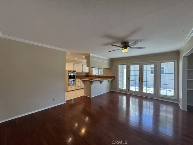 a view of an empty room with wooden floor and a kitchen
