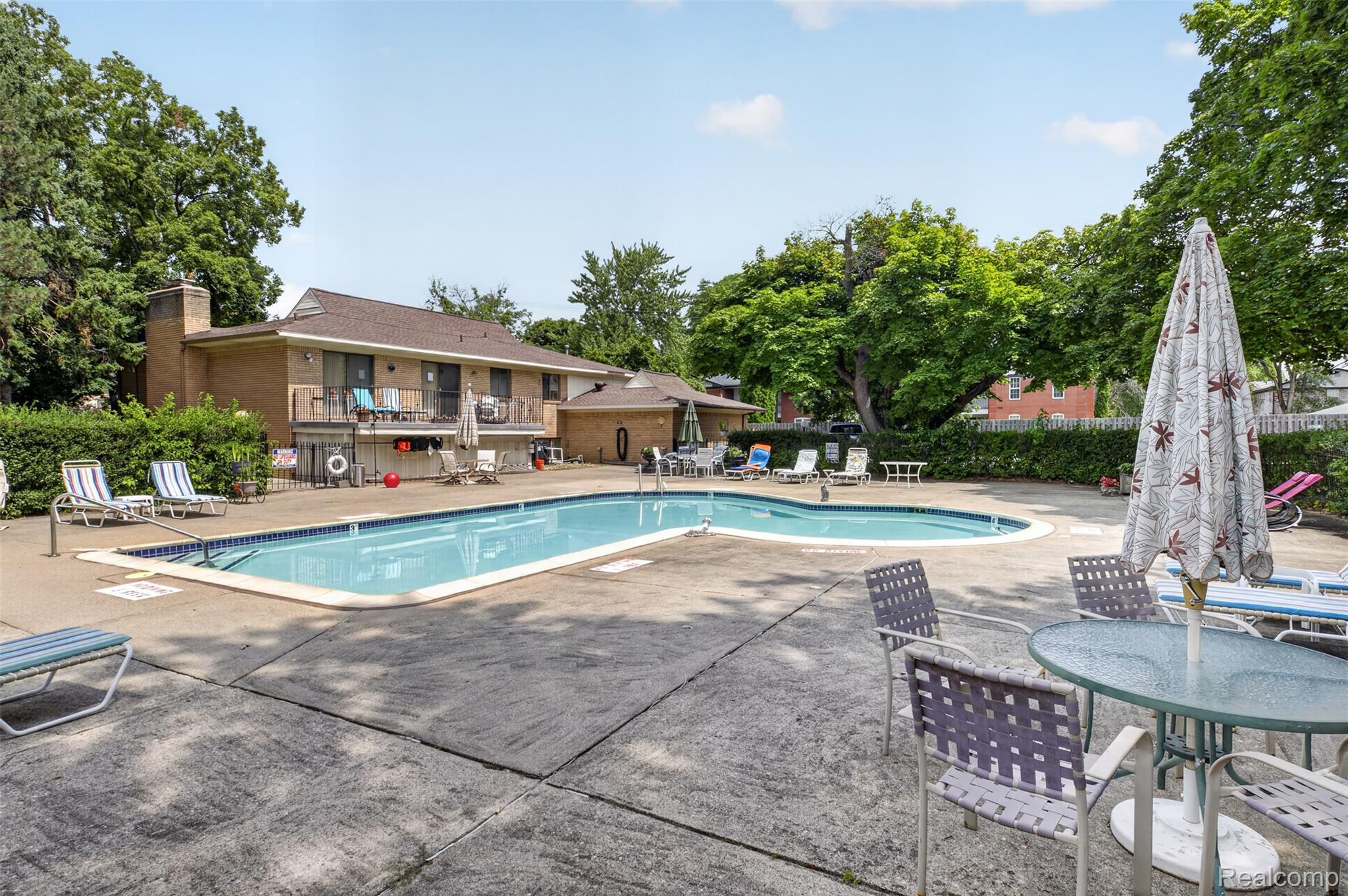 31915 West 14 Mile Road Farmington, MI 48334 - Photo 8 of 47 Outdoor swimming pool with concrete decking, surrounded by mature trees and a brick building with balconies