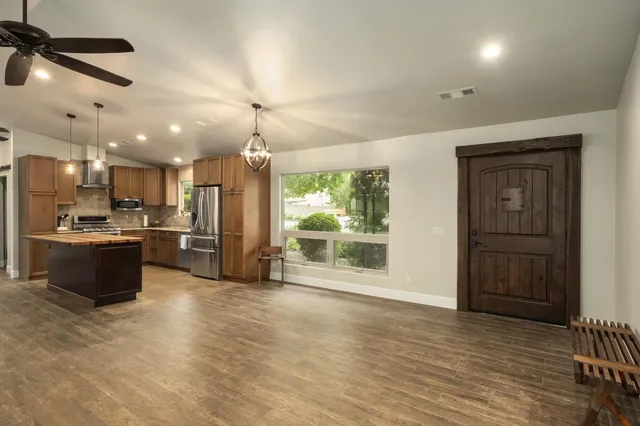 a kitchen with stainless steel appliances kitchen island granite countertop a refrigerator a sink a stove and oven with wooden floor