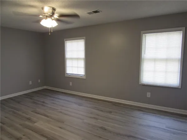an empty room with wooden floor fan and windows