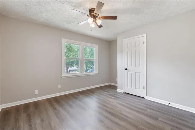 an empty room with wooden floor fan and windows