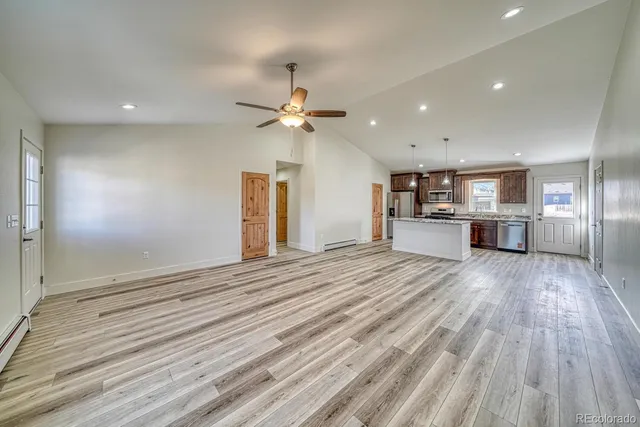 an empty room with wooden floor kitchen view and a window