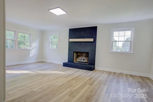 a view of an empty room with wooden floor fireplace and a window