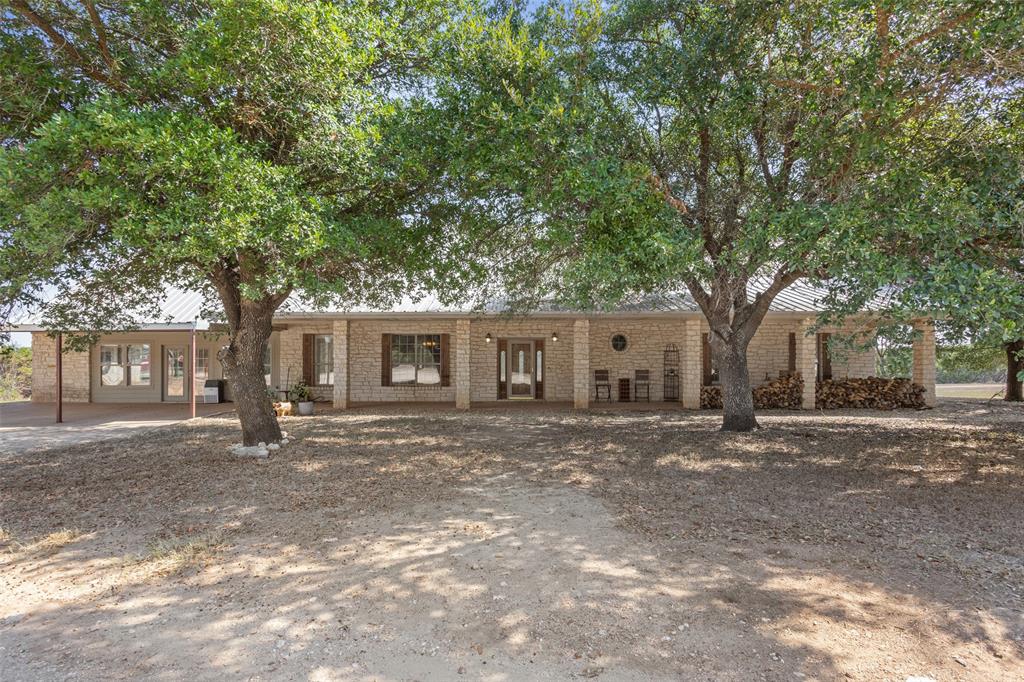 564 Sam Bass Road McGregor, TX 76657 - Photo 2 of 37 Expansive brick facade ranch-style residence featuring a metal roof, prominent mature trees, an inviting covered front porch, and substantial brick support columns