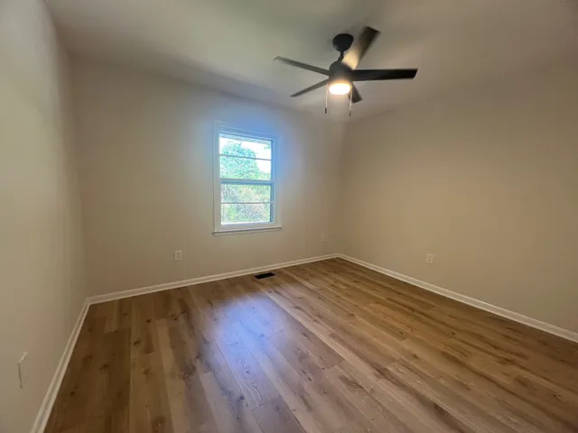 an empty room with wooden floor fan and windows