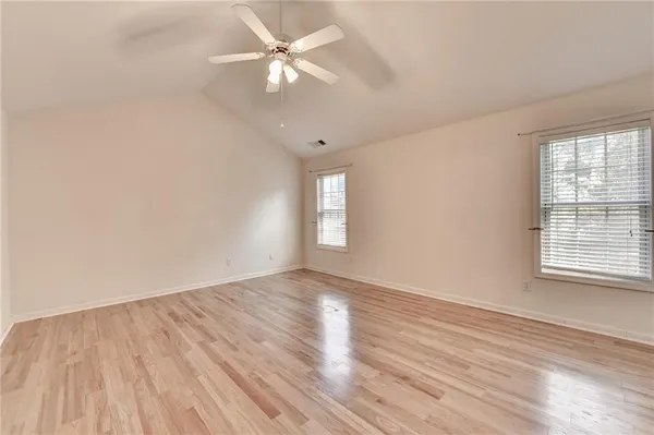 an empty room with wooden floor fan and windows