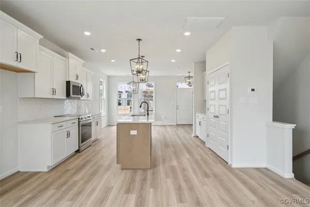 a large kitchen with stainless steel appliances a large counter top a stove a sink dishwasher and a refrigerator with wooden floor