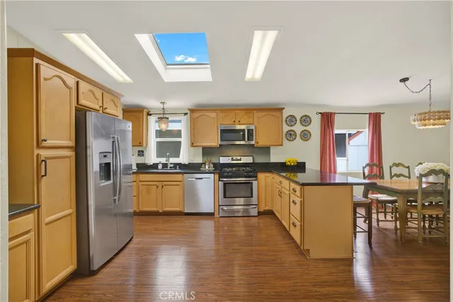 a large kitchen with stainless steel appliances a refrigerator a stove top oven a sink dishwasher and white cabinets with wooden floor