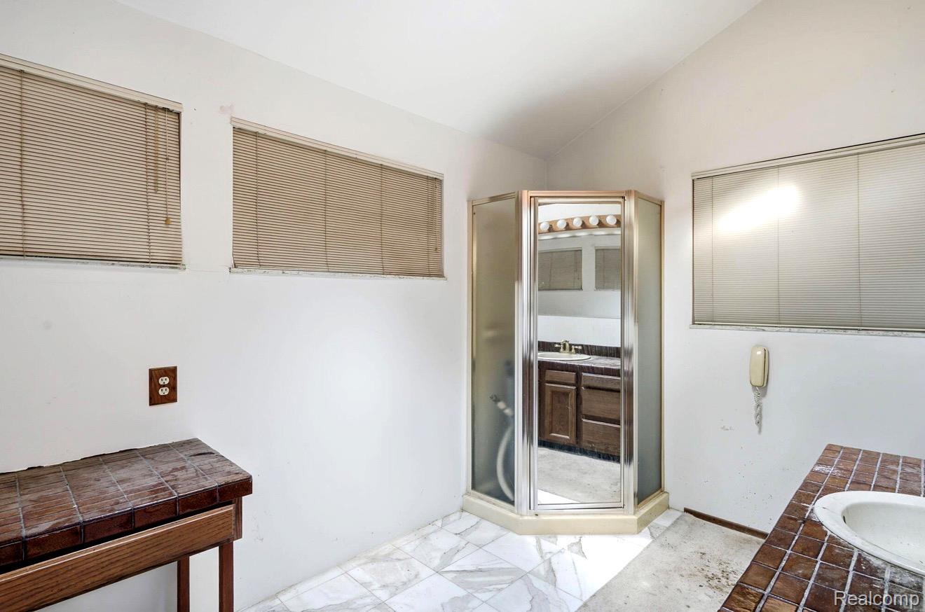 8890 Tipsico Lake Road Holly, MI 48442 - Photo 14 of 20 Corner glass-enclosed shower with a mirrored door, a dark wood-finish vanity with a light-toned countertop, and white tile flooring