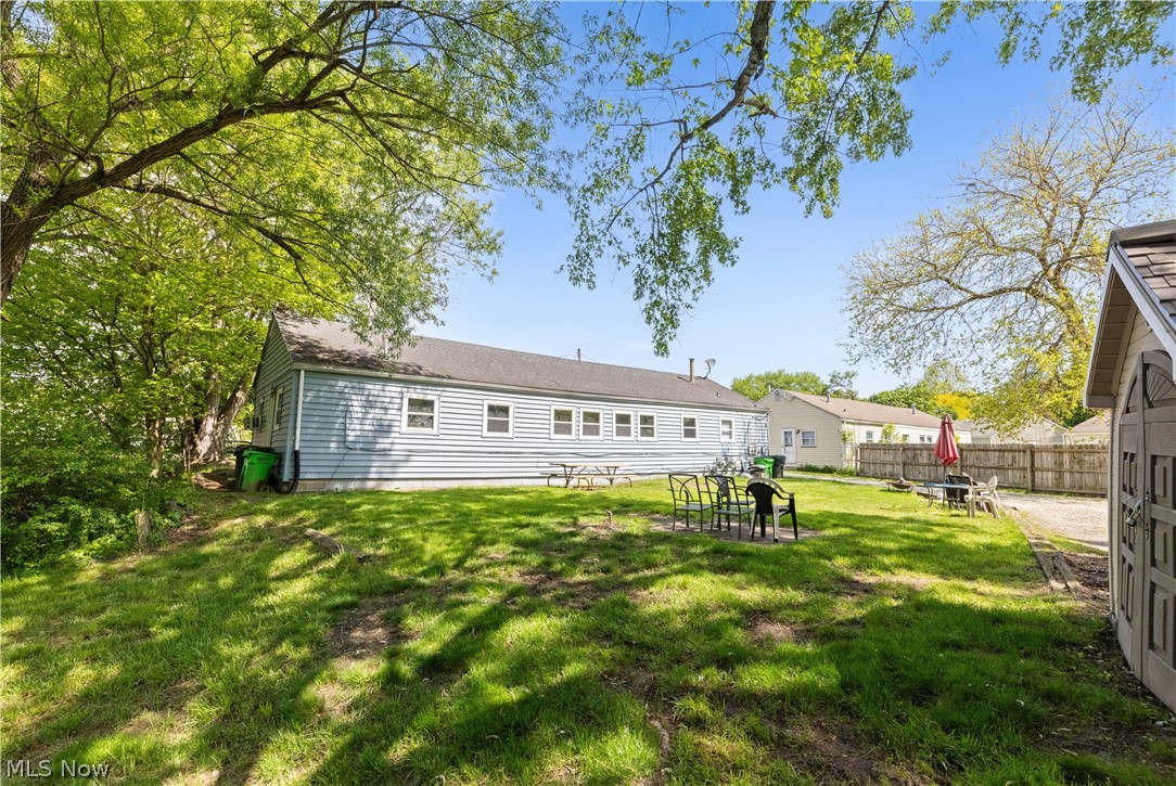 68-70 East Sunset Drive Rittman, OH 44270 - Photo 14 of 49 Spacious backyard featuring a large grassy area, mature trees, a wooden privacy fence, and a dedicated gravel area