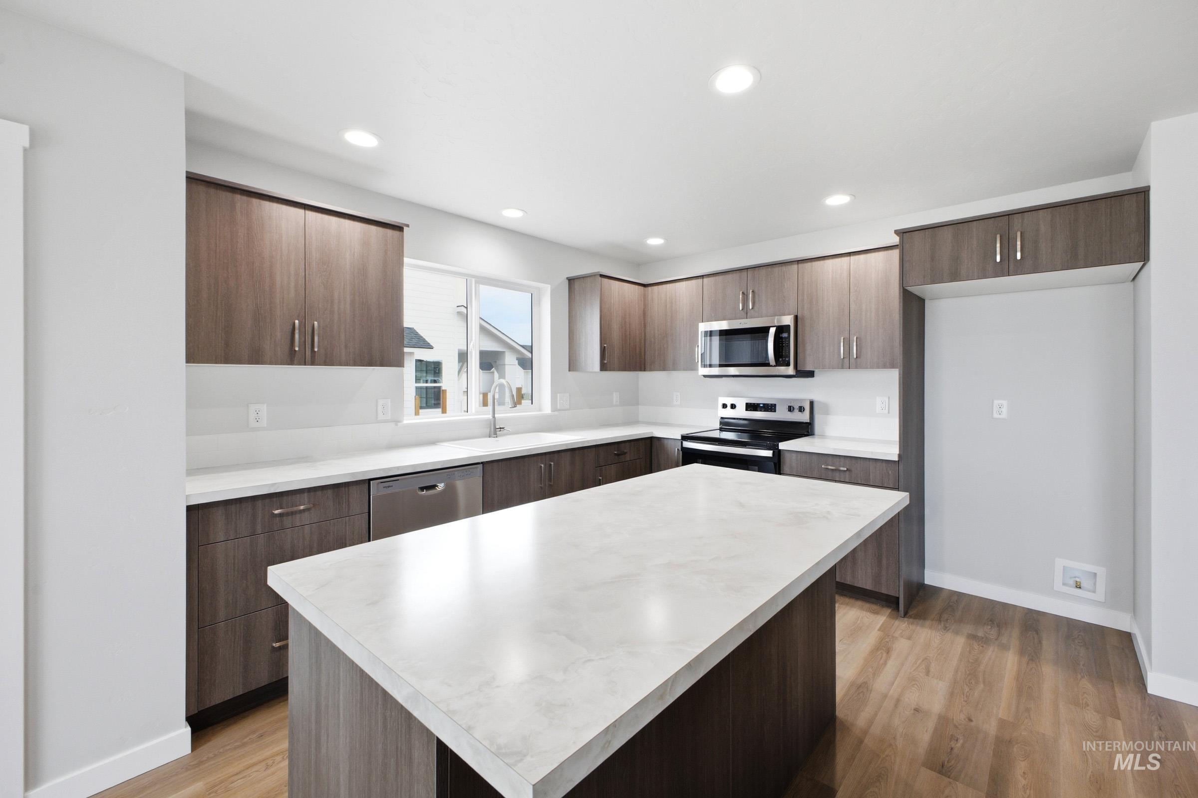 13702 Inman Court Caldwell, ID 83607 - Photo 3 of 23 Kitchen featuring stainless steel appliances, light wood-type flooring, light countertops, dark wood finish cabinets, and modern cabinets