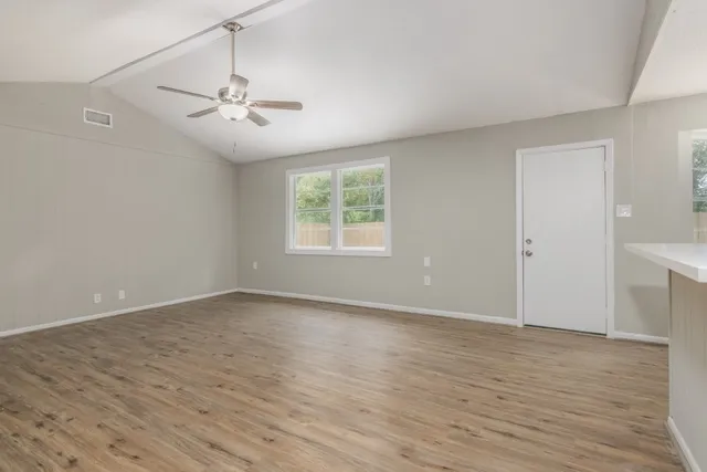an empty room with wooden floor chandelier fan and windows