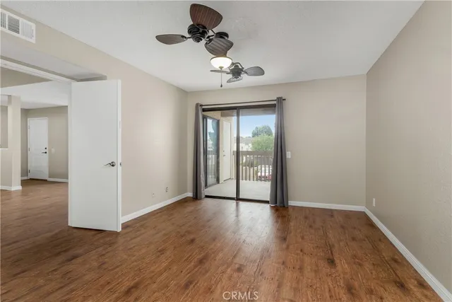 a view of an empty room with wooden floor and a ceiling fan
