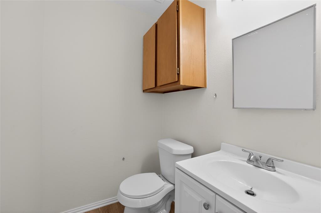 808 Park Street Commerce, TX 75428 - Photo 15 of 29 This bathroom features a white vanity with a sink and a chrome faucet, a white toilet, and a medicine cabinet with wooden doors