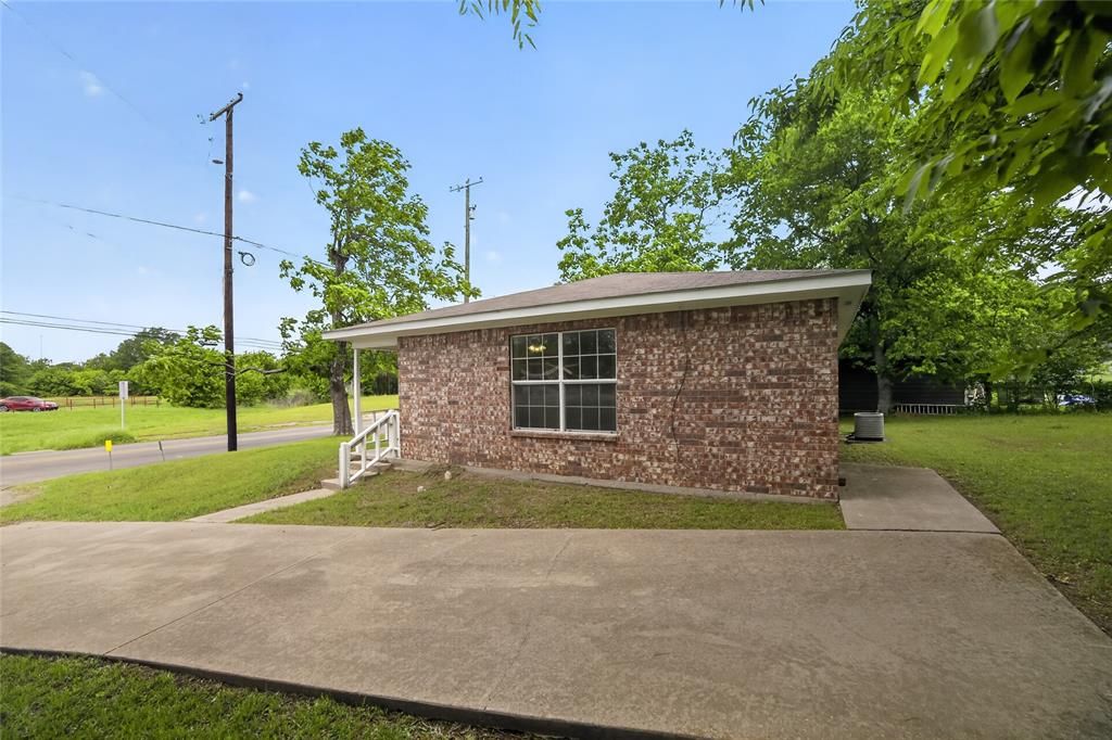 808 Park Street Commerce, TX 75428 - Photo 26 of 29 The property features a brick exterior with a pitched roof, a concrete driveway, and a well-maintained lawn
