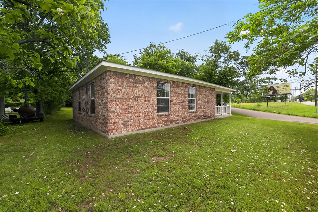 808 Park Street Commerce, TX 75428 - Photo 28 of 29 This property features a brick exterior, a covered front porch with white railings, and an expansive lawn with mature trees