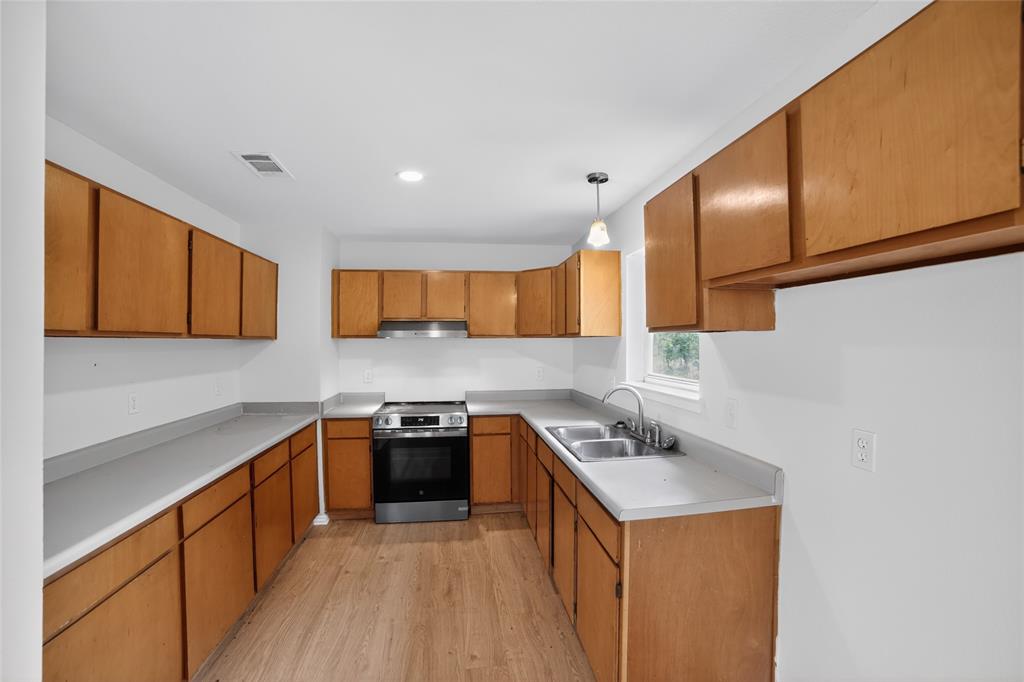 808 Park Street Commerce, TX 75428 - Photo 8 of 29 Kitchen featuring wood cabinetry, light-colored countertops, a stainless steel oven with an overhead range hood, and a double-basin stainless steel sink
