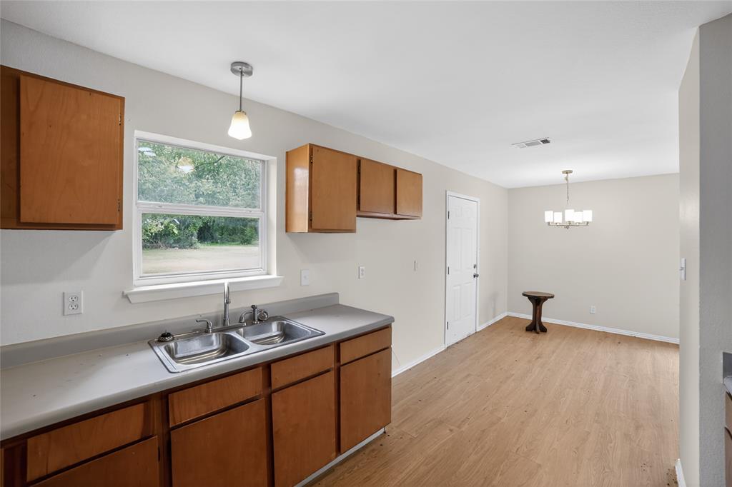 808 Park Street Commerce, TX 75428 - Photo 9 of 29 The property includes a kitchen with wood cabinetry, a double basin stainless steel sink, and light-colored countertops