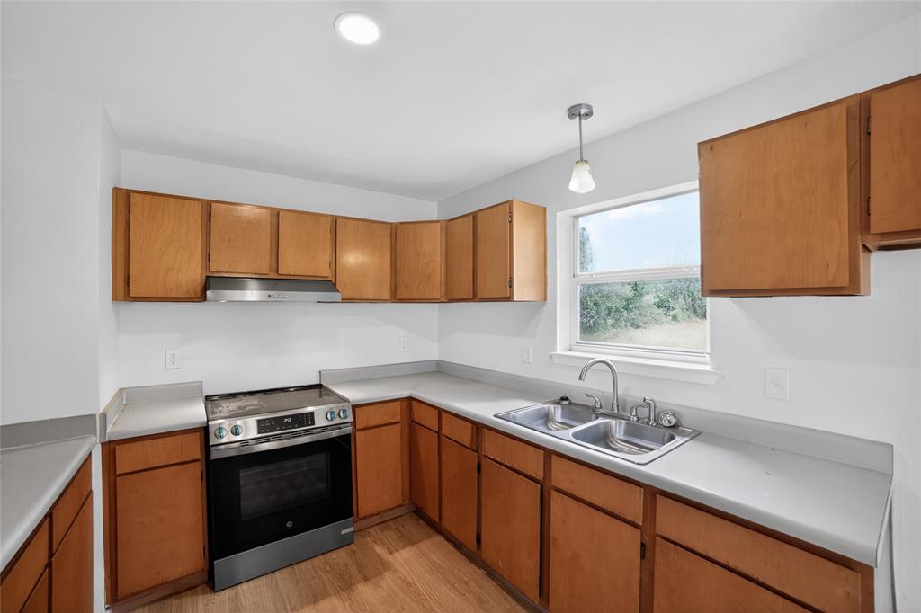 808 Park Street Commerce, TX 75428 - Photo 10 of 29 The kitchen features light wood cabinetry, a stainless steel range with a matching range hood, and a dual basin sink