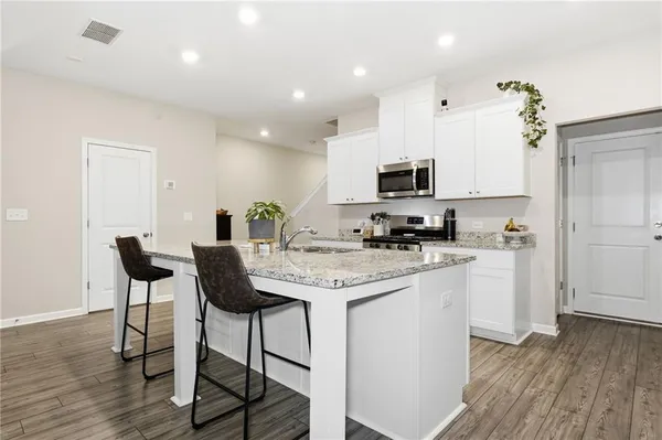 a kitchen with stainless steel appliances granite countertop a stove top oven a sink a dining table and chairs with wooden floor