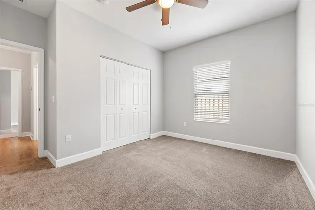 an empty room with chandelier fan and windows