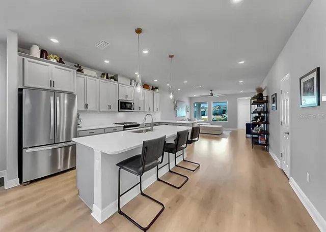 a kitchen with stainless steel appliances kitchen island granite countertop a refrigerator a stove a sink a dining table and chairs with wooden floor