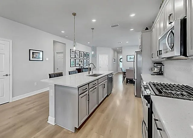 a kitchen with stainless steel appliances granite countertop a stove a sink a refrigerator and white cabinets with wooden floor