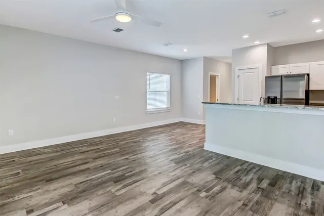 an empty room with wooden floor and kitchen view