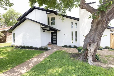 a view of a white house next to a yard with big trees