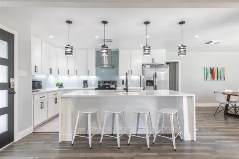 a kitchen with stainless steel appliances kitchen island granite countertop a dining table chairs and white cabinets