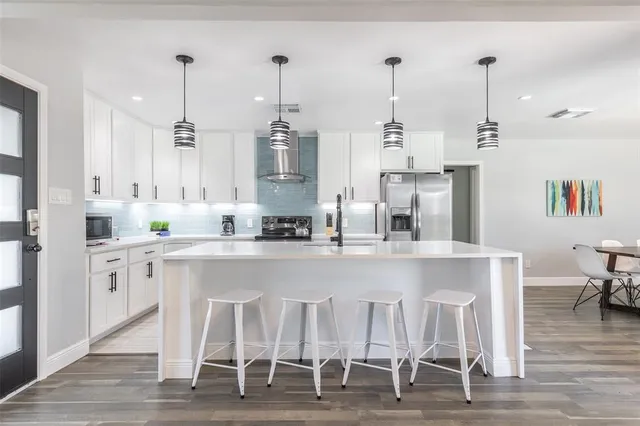 a kitchen with stainless steel appliances kitchen island granite countertop a dining table chairs and white cabinets