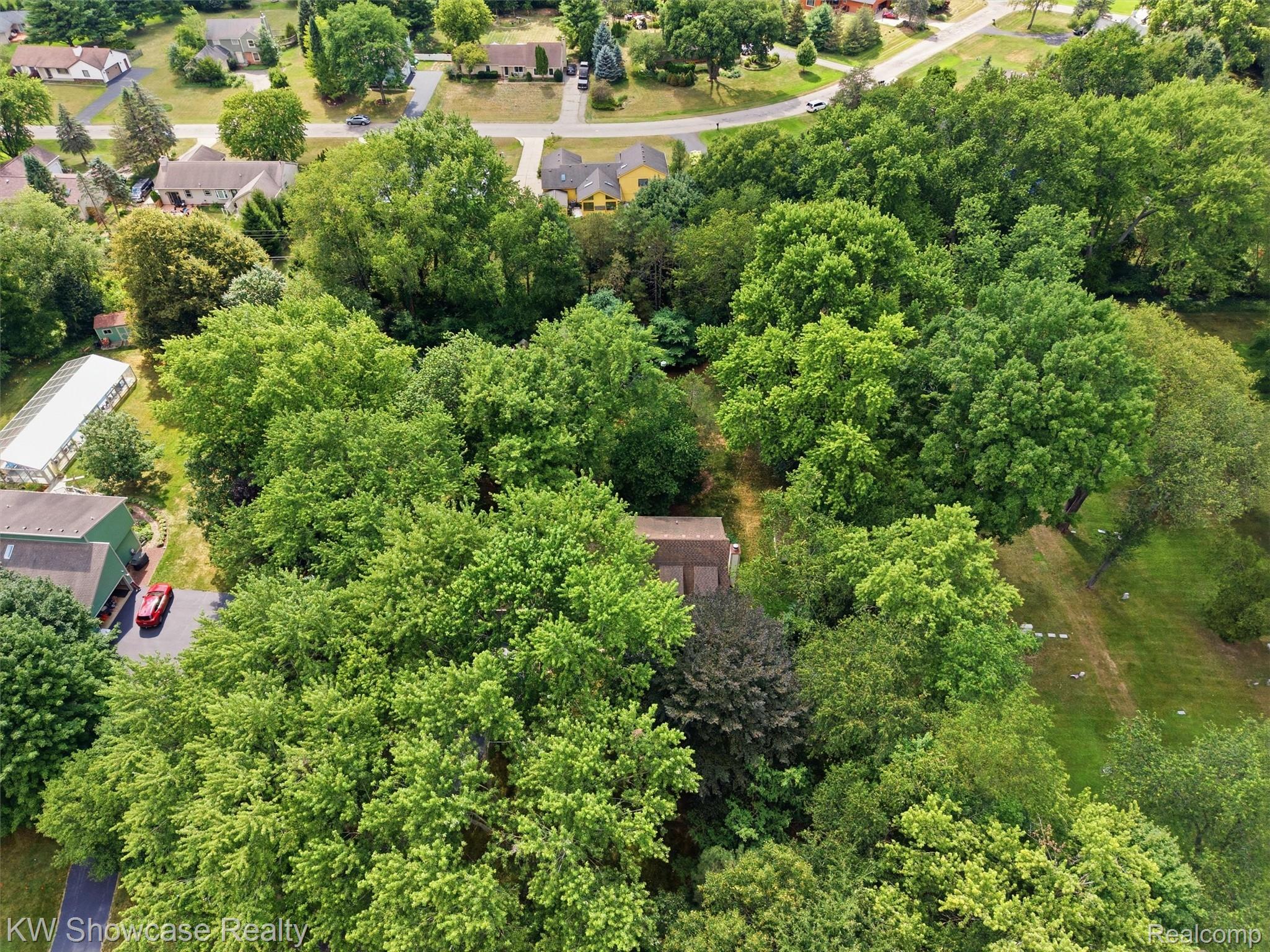 3360 Pleasant Valley Road Brighton, MI 48114 - Photo 56 of 60 Expansive treed lot featuring a partially visible residence with a brown roof, surrounded by mature deciduous trees