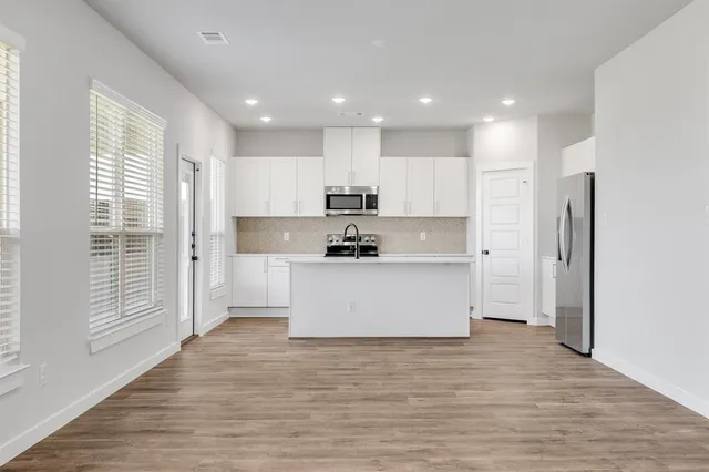 a view of kitchen with granite countertop refrigerator oven sink and white cabinets with wooden floor