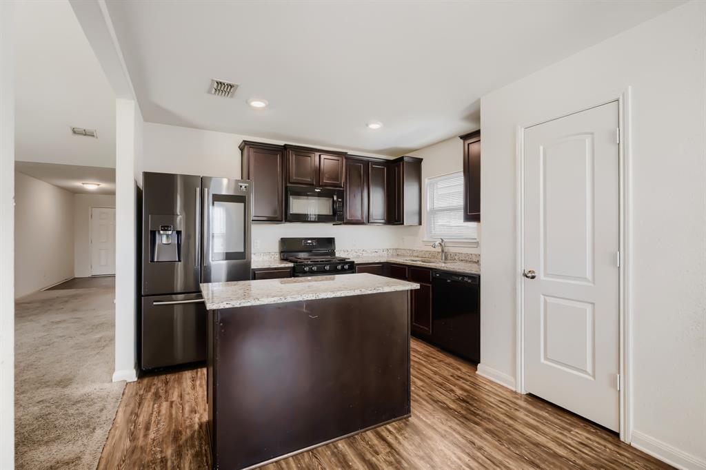 4309 Cat Tail Way Forney, TX 75126 - Photo 12 of 30 Kitchen featuring wood-finish flooring, dark wood cabinetry, a central island with a light-toned countertop, and stainless steel appliances