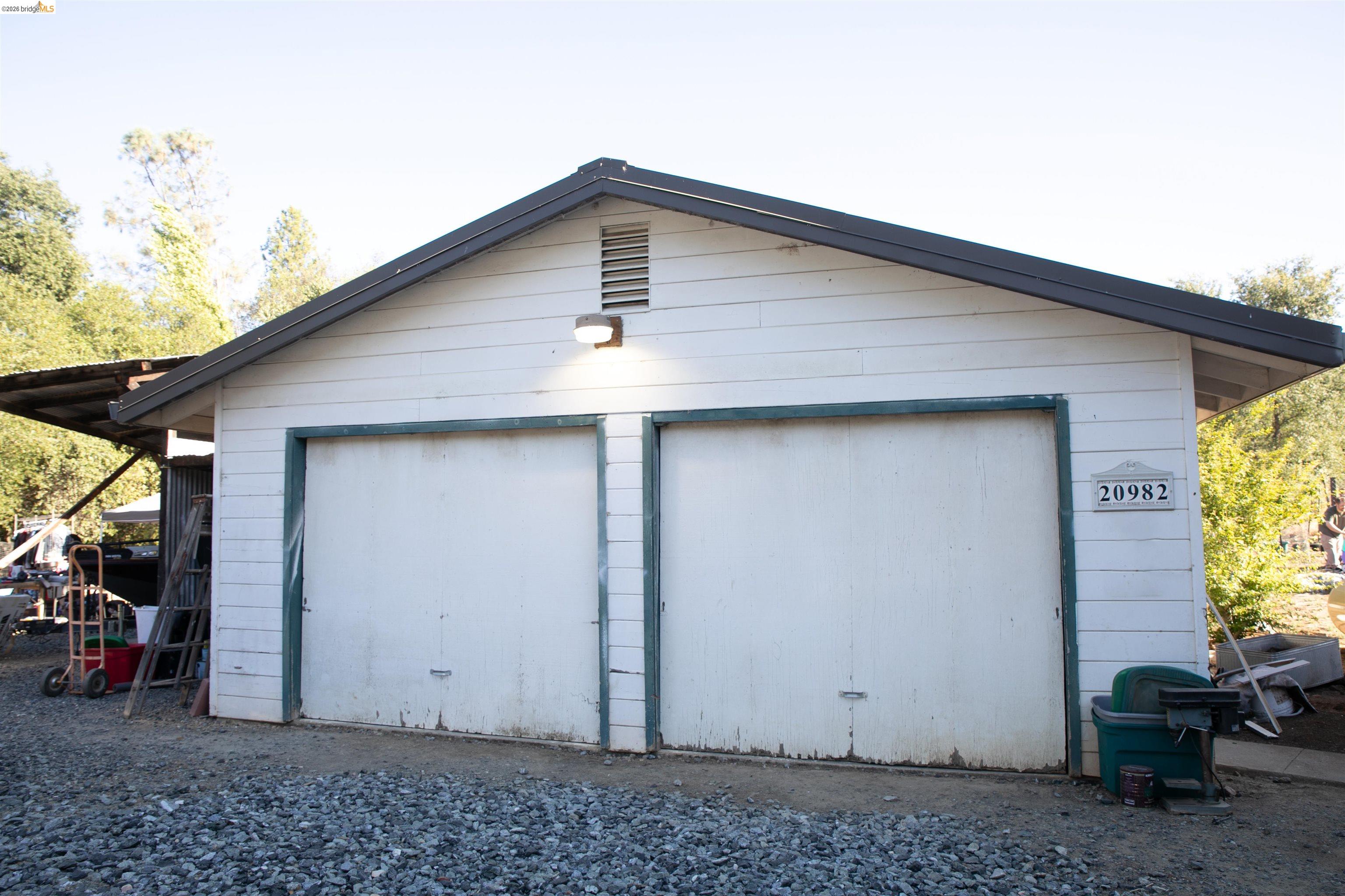 20982 Shaws Flat Road Sonora, CA 95370 - Photo 6 of 26 Two-car garage with white siding, a dark roof, and two individual garage doors with green trim
