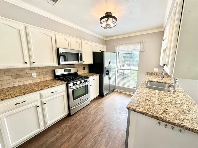 a kitchen with stainless steel appliances granite countertop a stove top oven a sink dishwasher and a microwave oven on the wooden floor